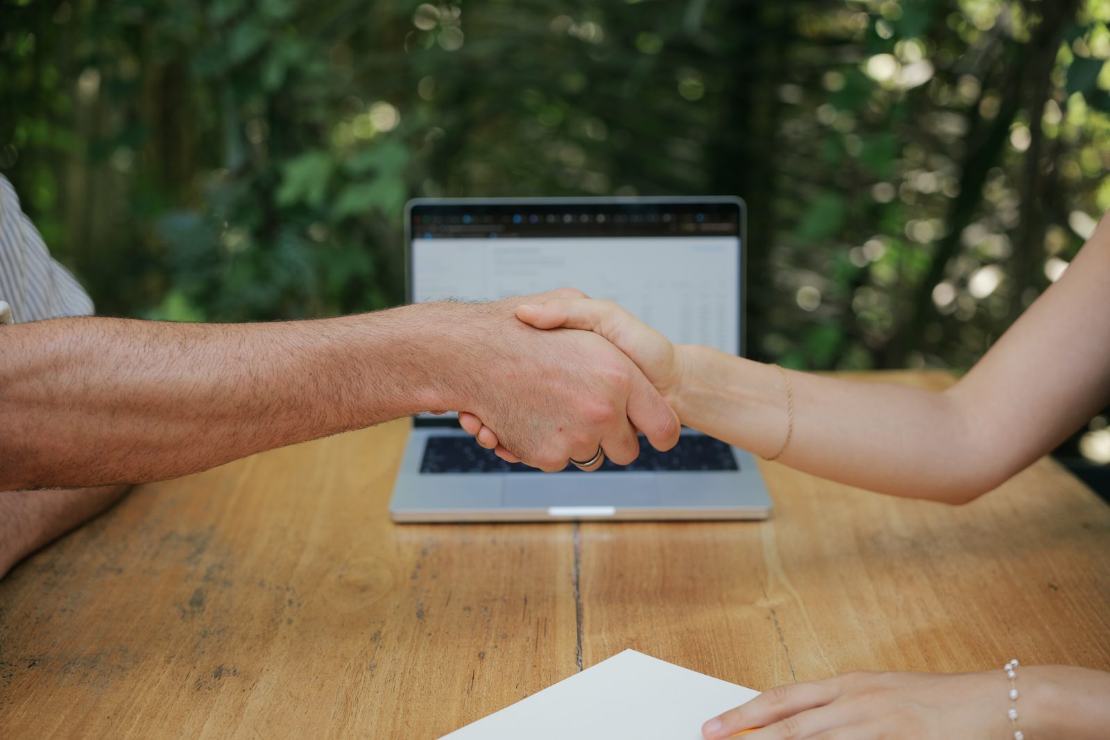 A handshake across the table in front of a laptop, the True Tally accountability partnership